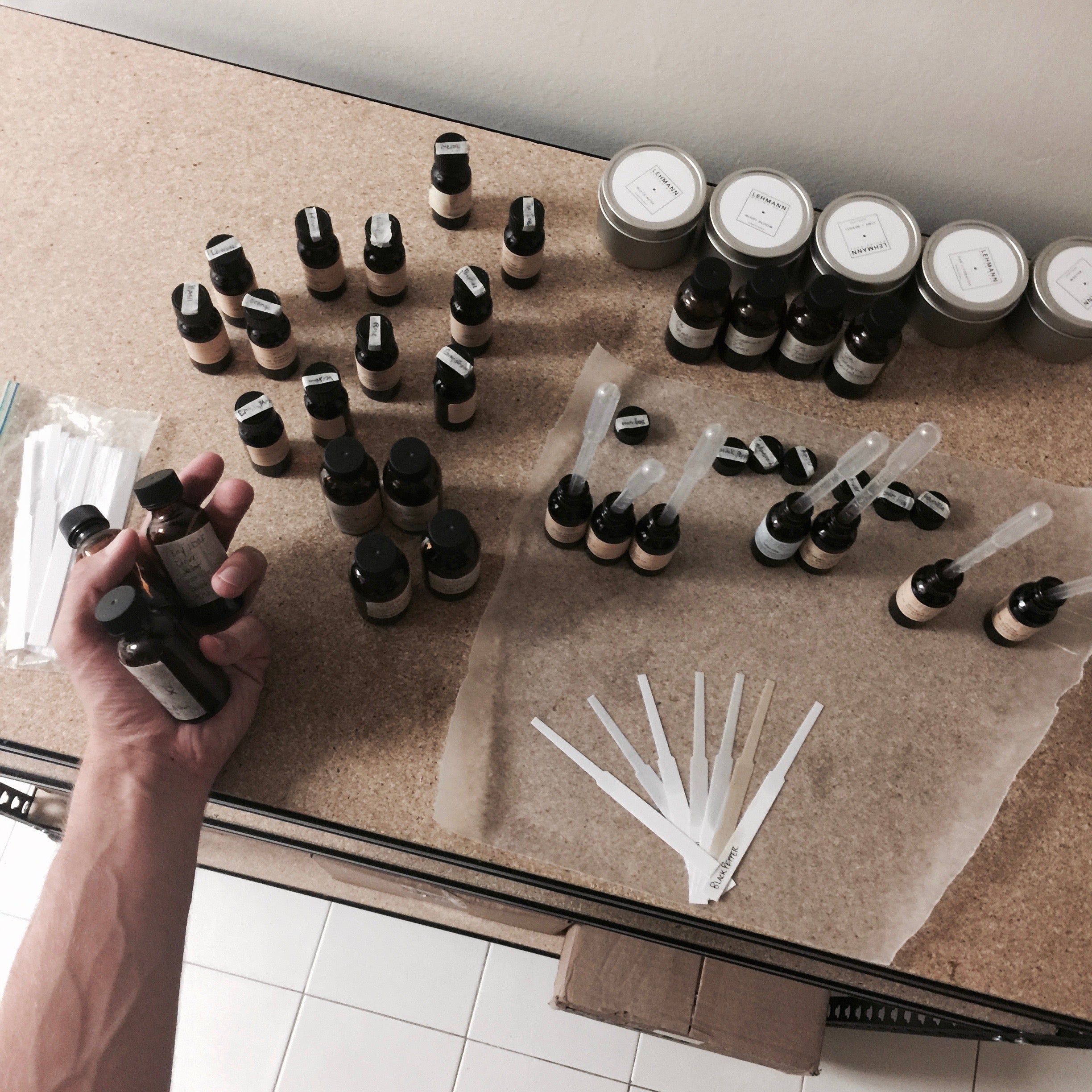 Hand holding 3 small amber glass bottles on table full of more small amber glass bottles and fragrance paper strips